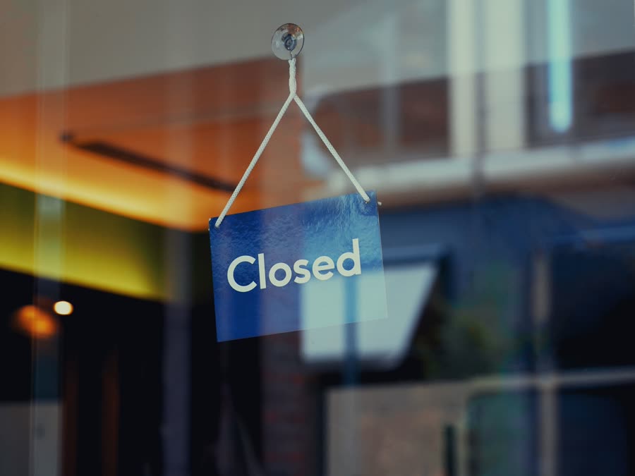 A "Closed" sign hanging in a restaurant's front window at night.